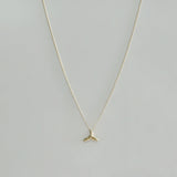 Delicate 14K gold whale tail charm on fine chain – laid flat on beige surface