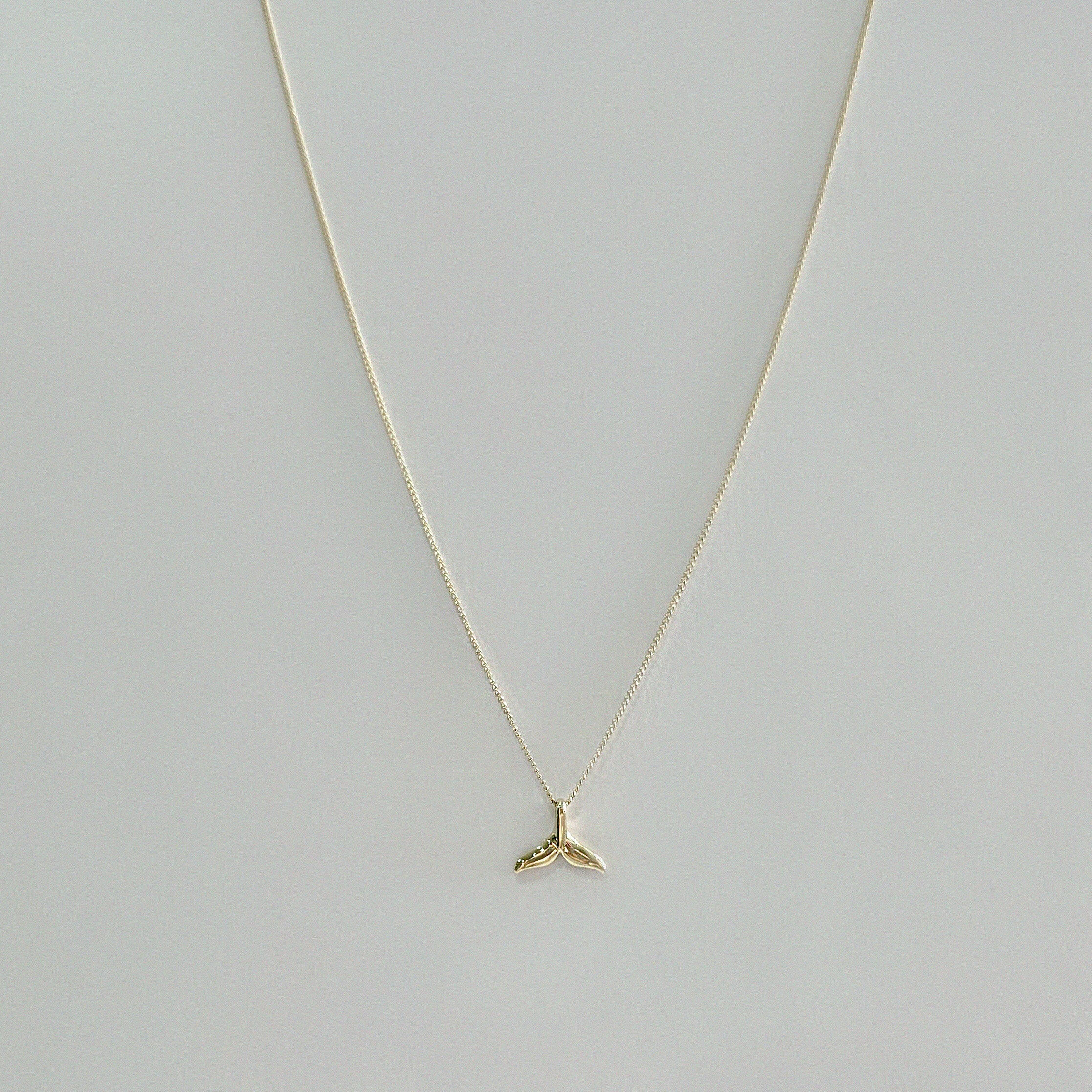 Delicate 14K gold whale tail charm on fine chain – laid flat on beige surface