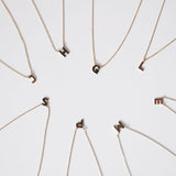 Multiple initial necklaces, including J, H, G, L. E, M, P and S, displayed with their chains against a clean white backdrop