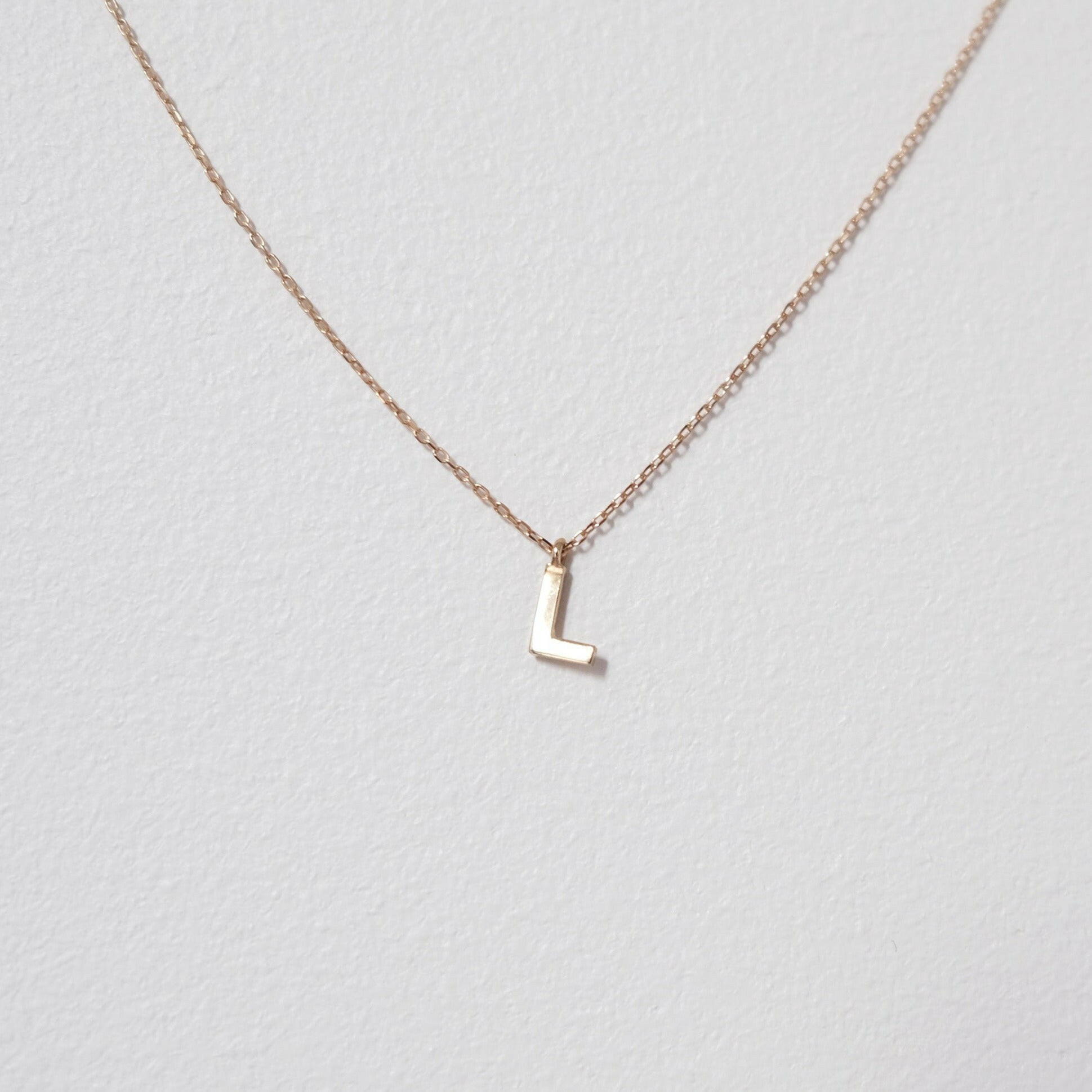 Refined close-up of the letter L pendant in 10K solid gold, photographed with chain slightly out of focus