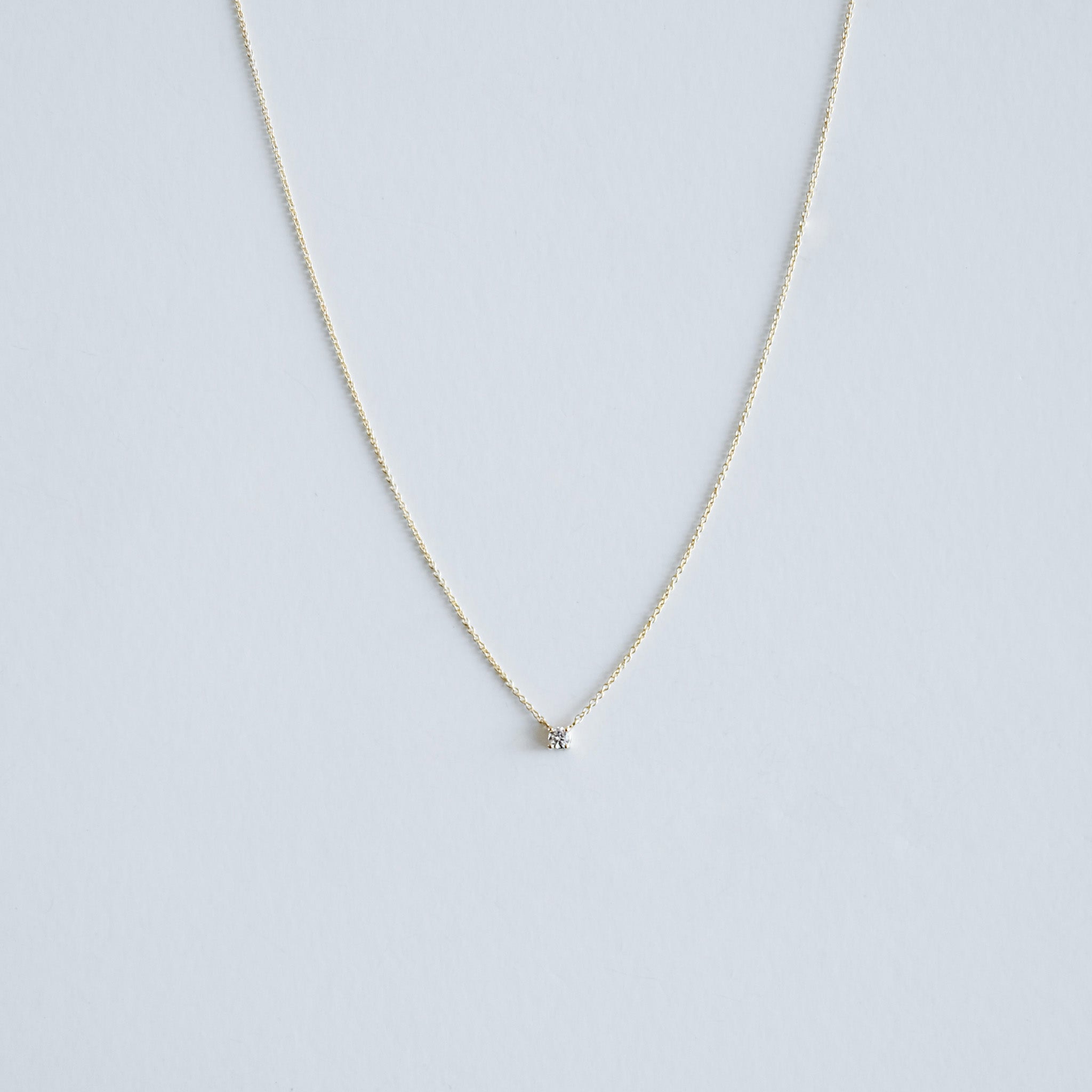 Gold necklace with a small diamond pendant on a light gray background