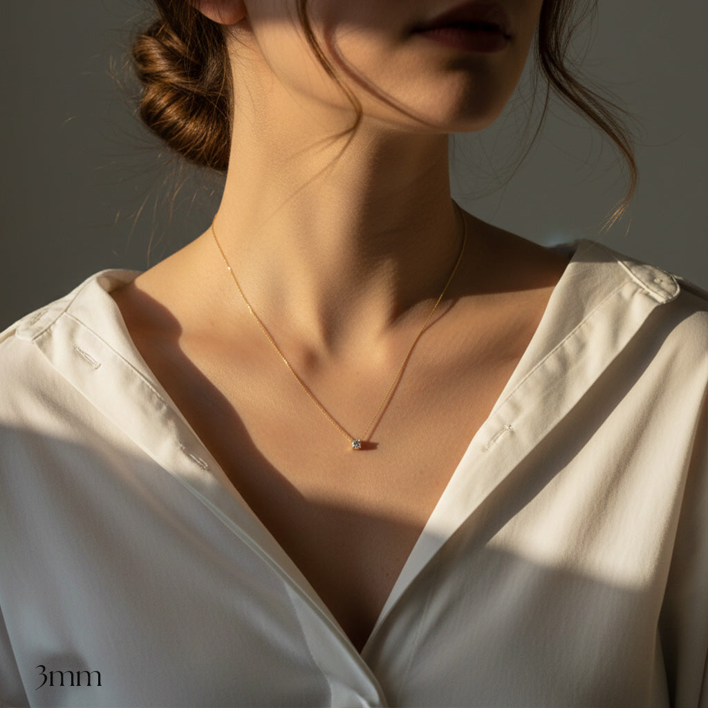 Necklace with a small pendant worn by a person in a white shirt, with a neutral background.