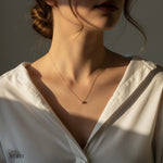 Necklace with a small pendant worn by a person in a white shirt, with a neutral background.