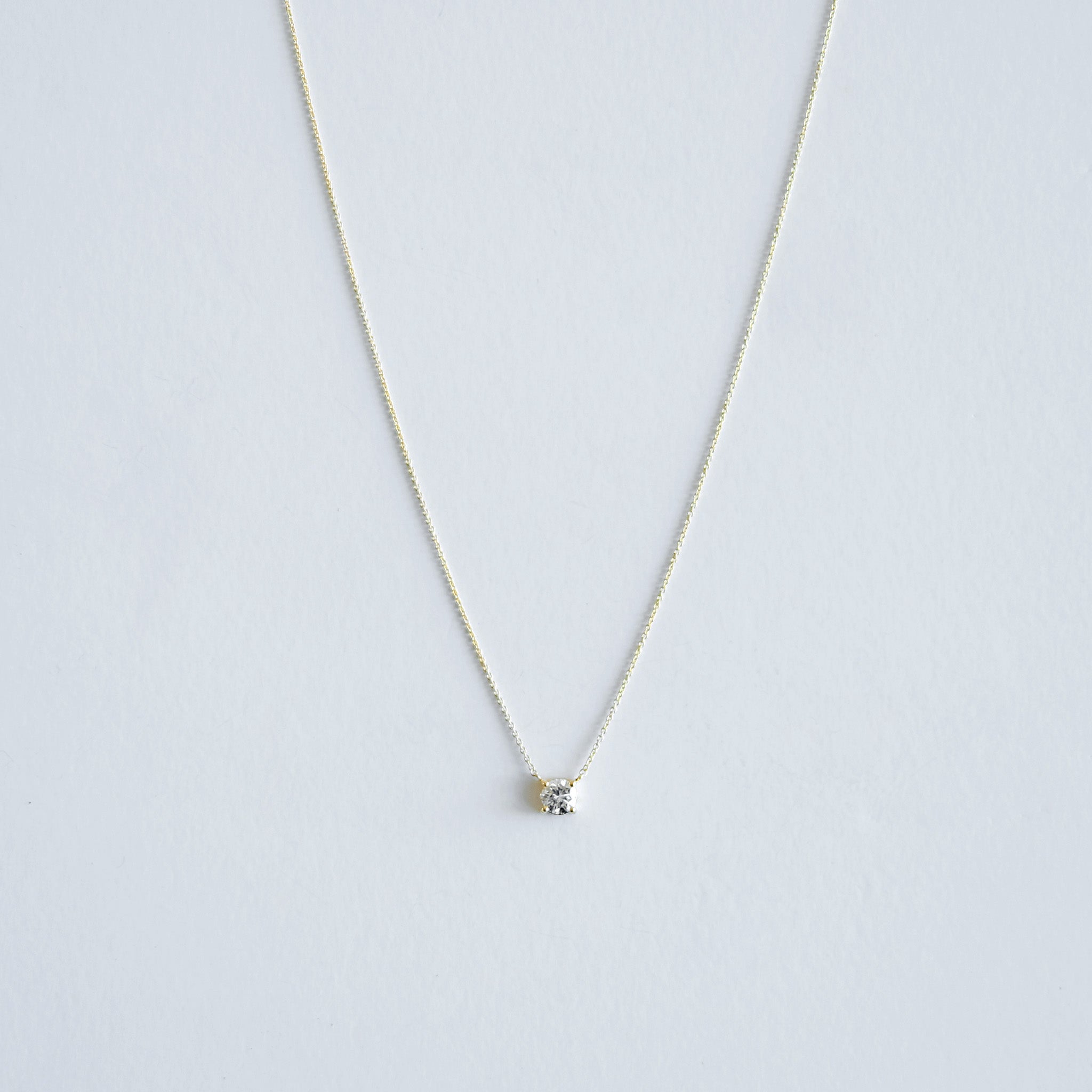 Gold necklace with a small pendant on a light gray background