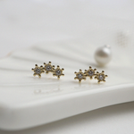 Close up shot of gold earrings featuring three petite cubic zirconia flowers