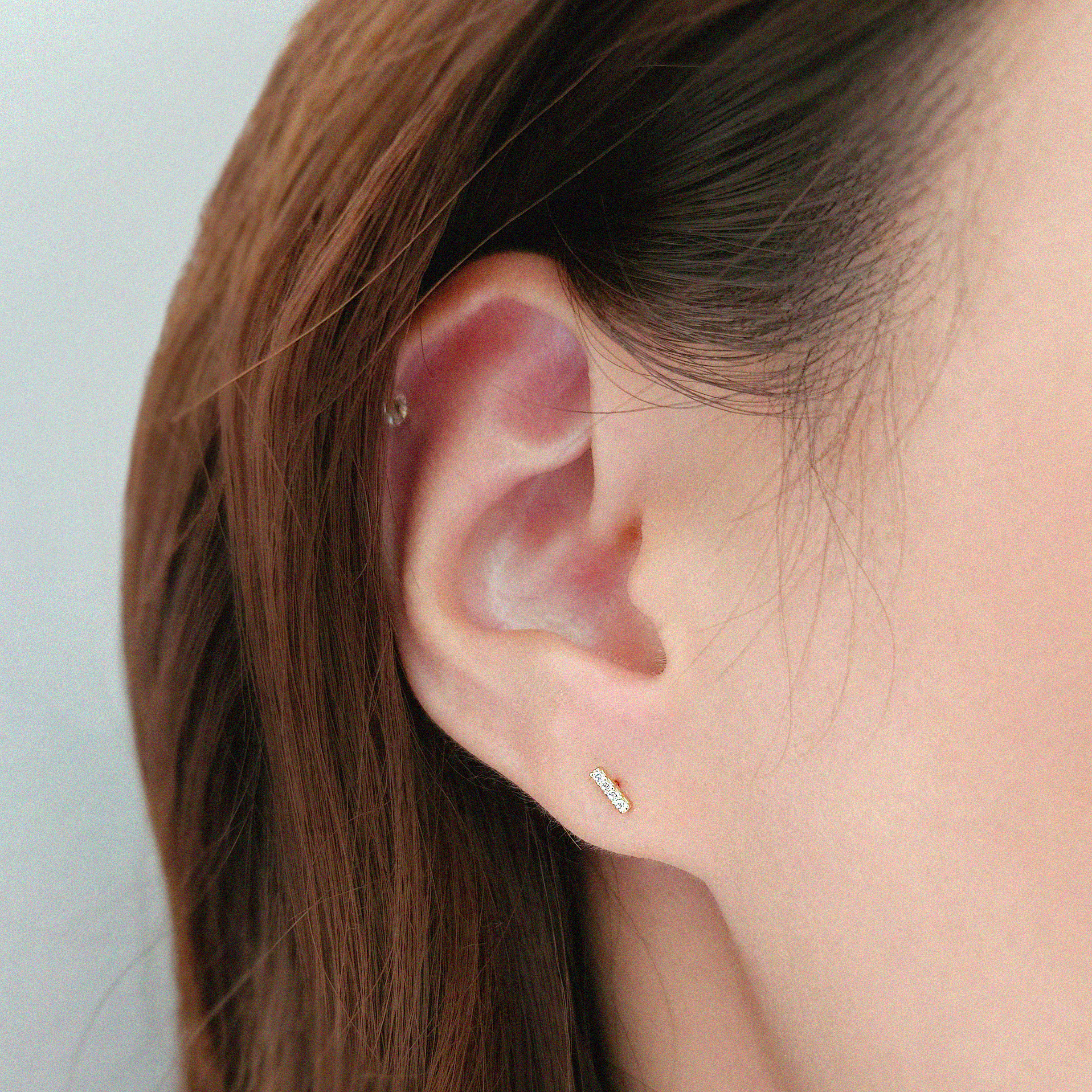 Slim gold bar studs styled on ear with other earrings