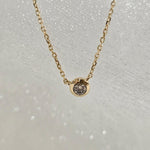 Overhead view of single round diamond set in a minimal 14K gold bezel pendant
