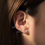 Close-up of an ear wearing three diamond stud earrings with size labels.