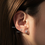 Close-up of an ear wearing three diamond stud earrings with size labels.