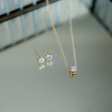 Gold necklace and earrings with diamond stones on a reflective surface
