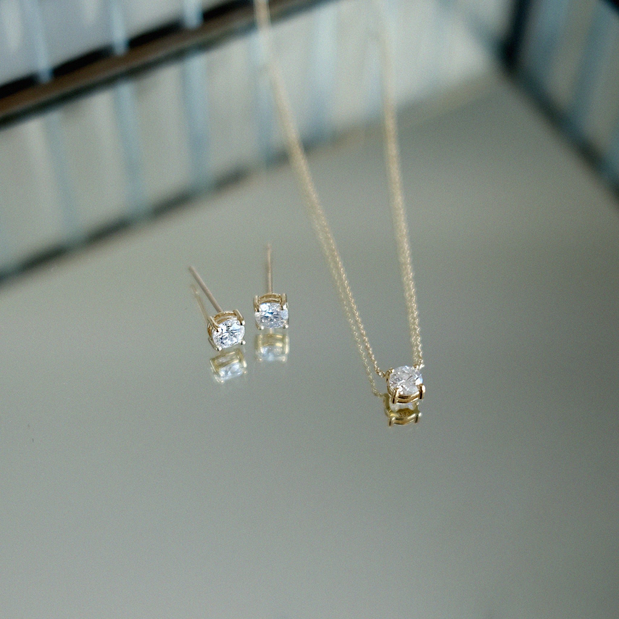 Gold necklace and earrings with diamond stones on a reflective surface
