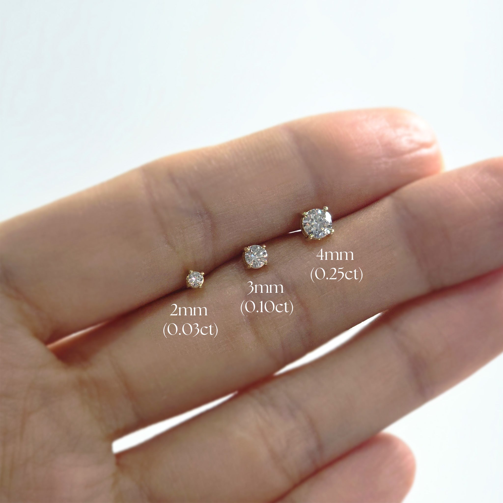 Diamond earrings of different sizes held on a hand with measurements displayed.