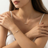 Woman wearing a gold necklace and bracelet on a neutral background
