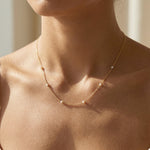 Close-up of a person wearing a delicate gold necklace with small beads.