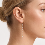 Close-up of a woman wearing a gold earring with clear stones on a plain background