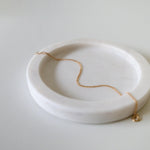 Fine gold bracelet laid on soft beige tray with curved edges
