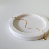 Fine gold bracelet laid on soft beige tray with curved edges