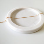 Fine gold bracelet laid on soft beige tray with curved edges