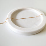 Fine gold bracelet laid on soft beige tray with curved edges