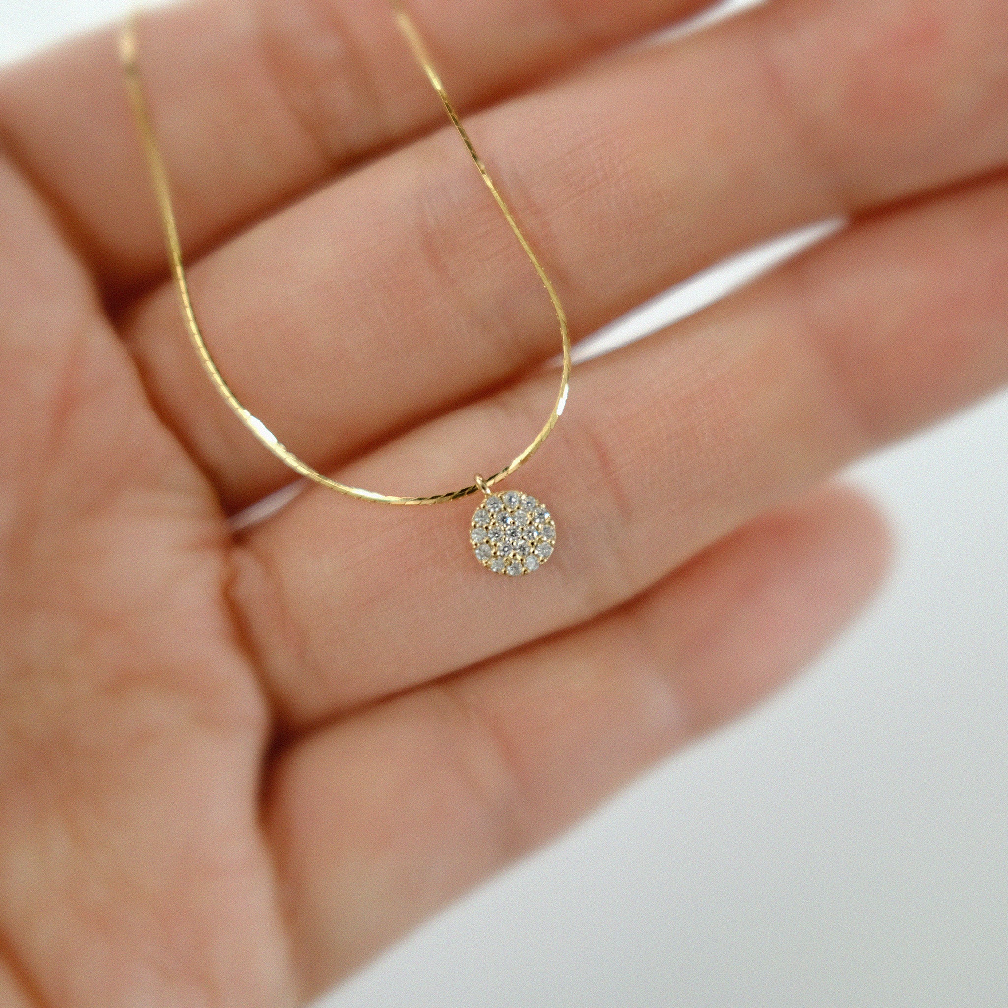 Gold necklace with a diamond pendant held in a hand against a white background