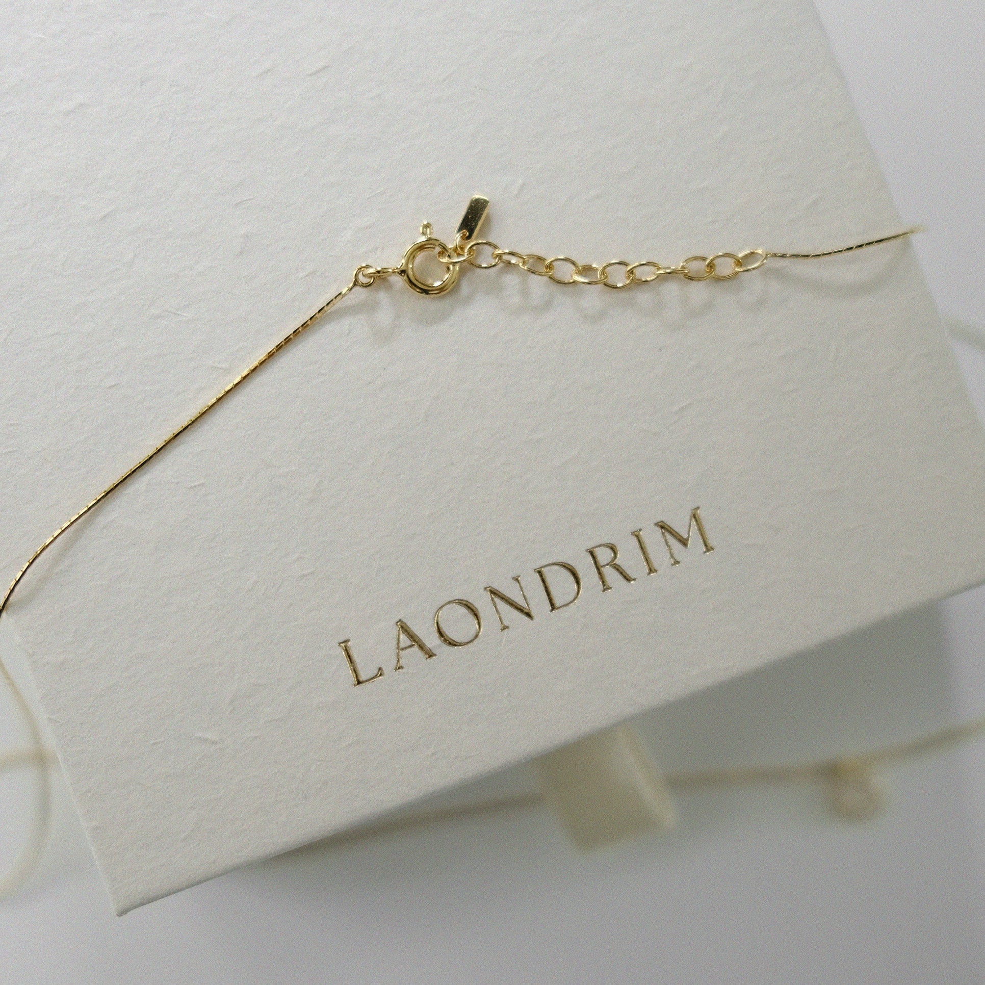 Gold bracelet on a white stand with 'LAONDRIM' branding.