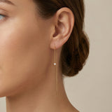 Close-up of a woman wearing a gold chain earring with a pearl drop on a neutral background