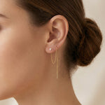 Close-up of an ear wearing a gold earring with a pearl, against a neutral background.