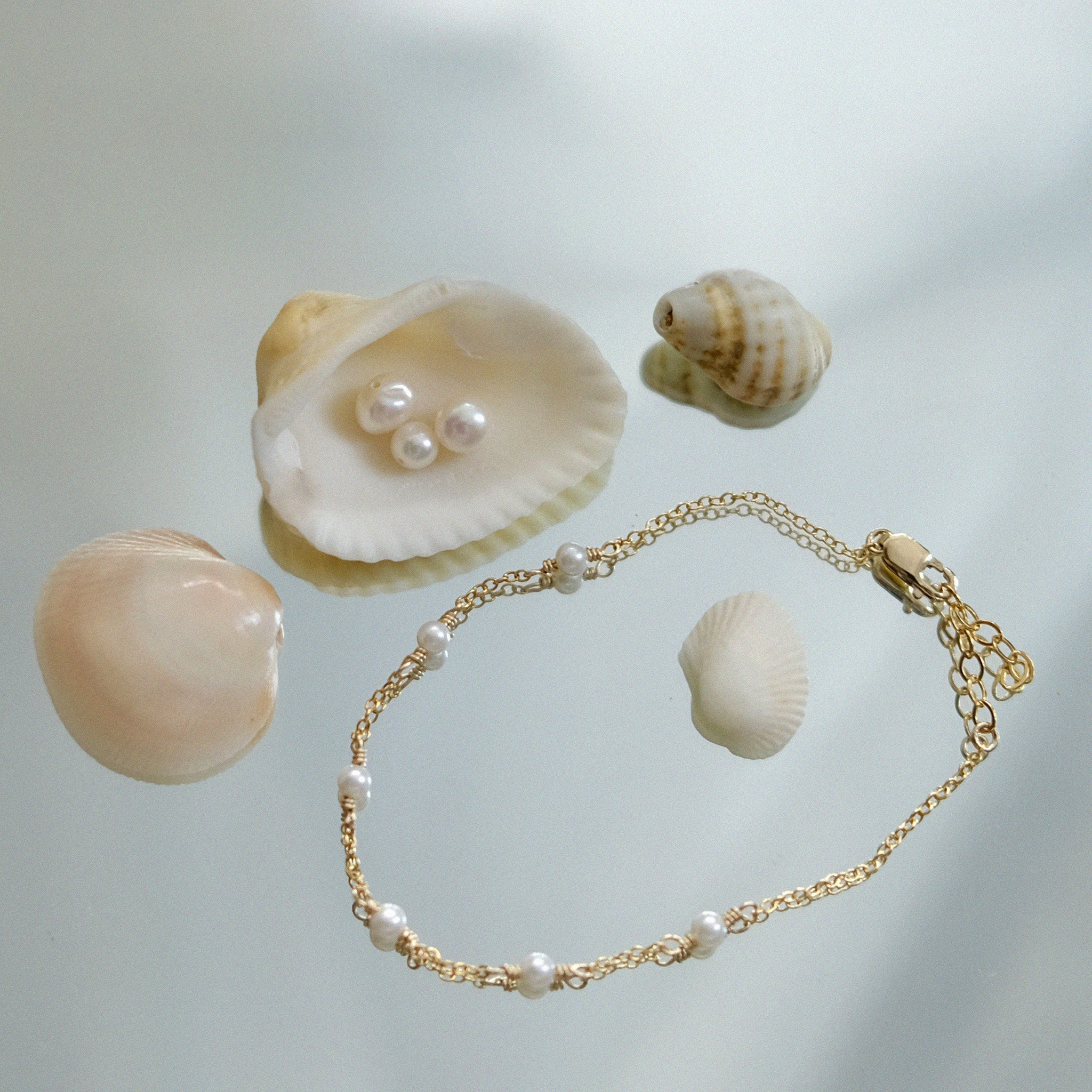 Gold bracelet with pearls and seashells on a light background
