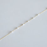 Delicate gold chain with small pearls bracelet on a light gray background