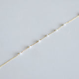Delicate gold chain with small pearls bracelet on a light gray background