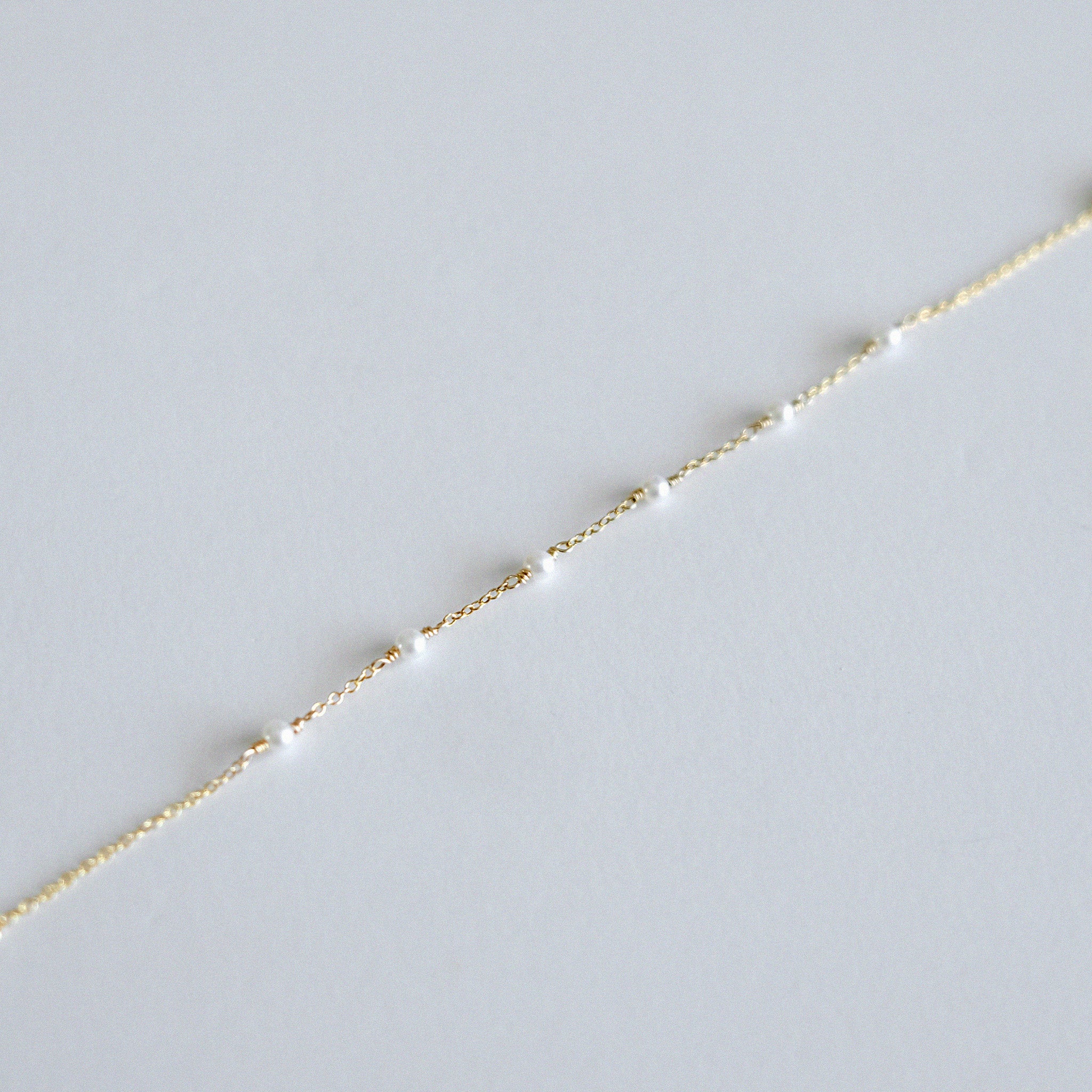 Delicate gold chain with small pearls bracelet on a light gray background