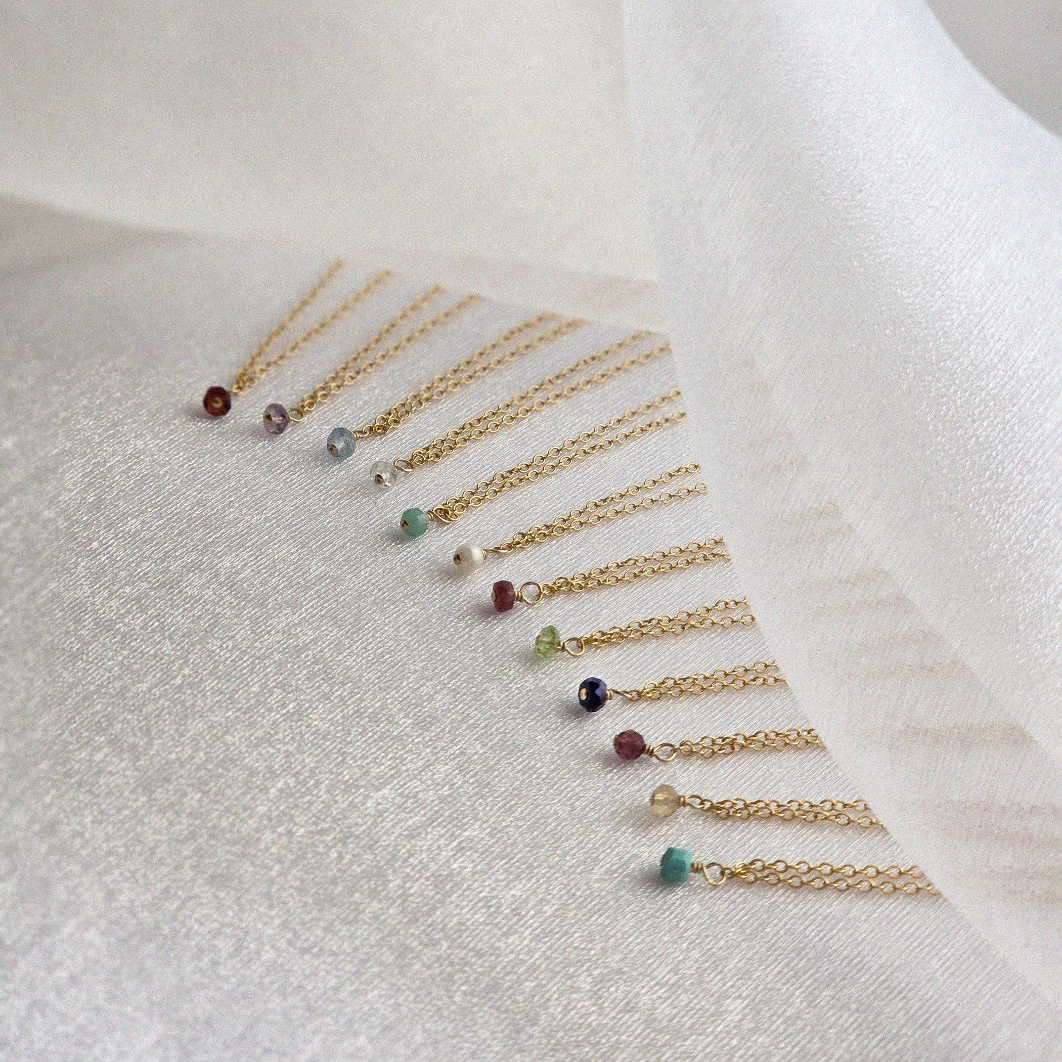 Set of gold necklaces with small gemstones on a white fabric background