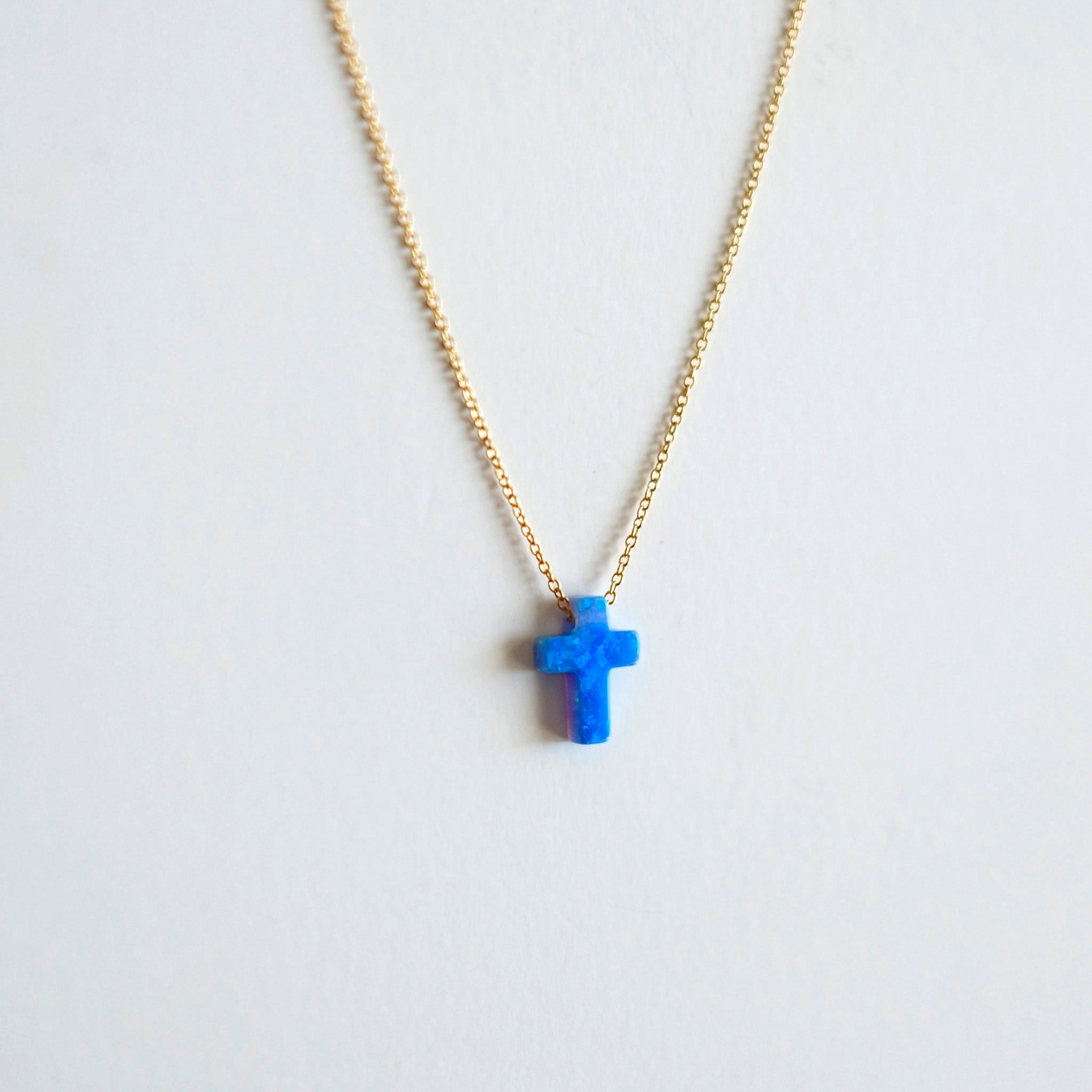 Necklace with a blue opal cross pendant on a light gray background