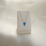 Necklace with a blue cross pendant on a white stand against a light background
