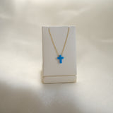 Necklace with a blue cross pendant on a white stand against a light background