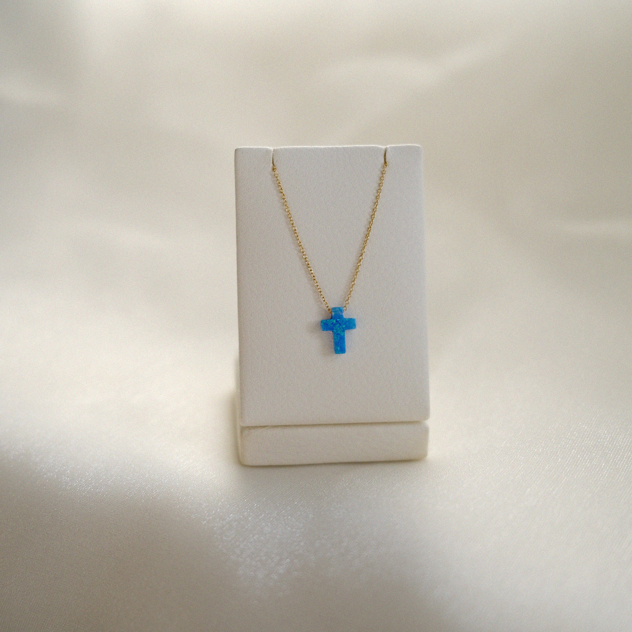 Necklace with a blue cross pendant on a white stand against a light background