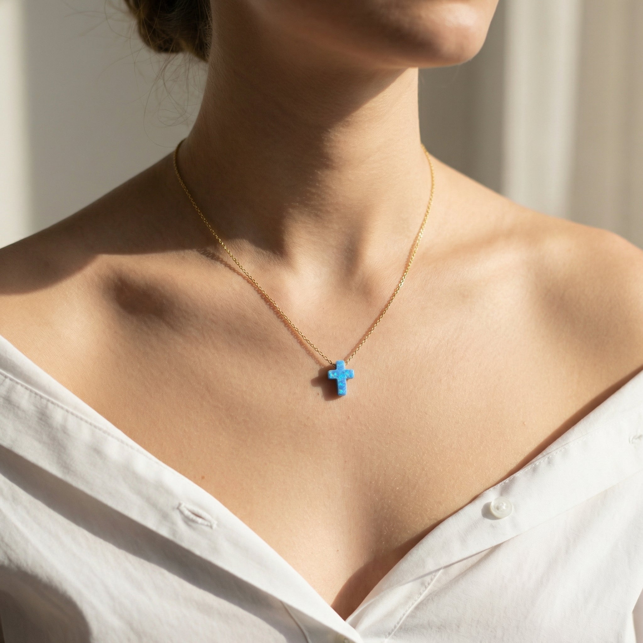 Necklace with a blue cross pendant worn by a person in a white shirt.