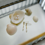 Gold earrings with pearls on a white surface with seashells