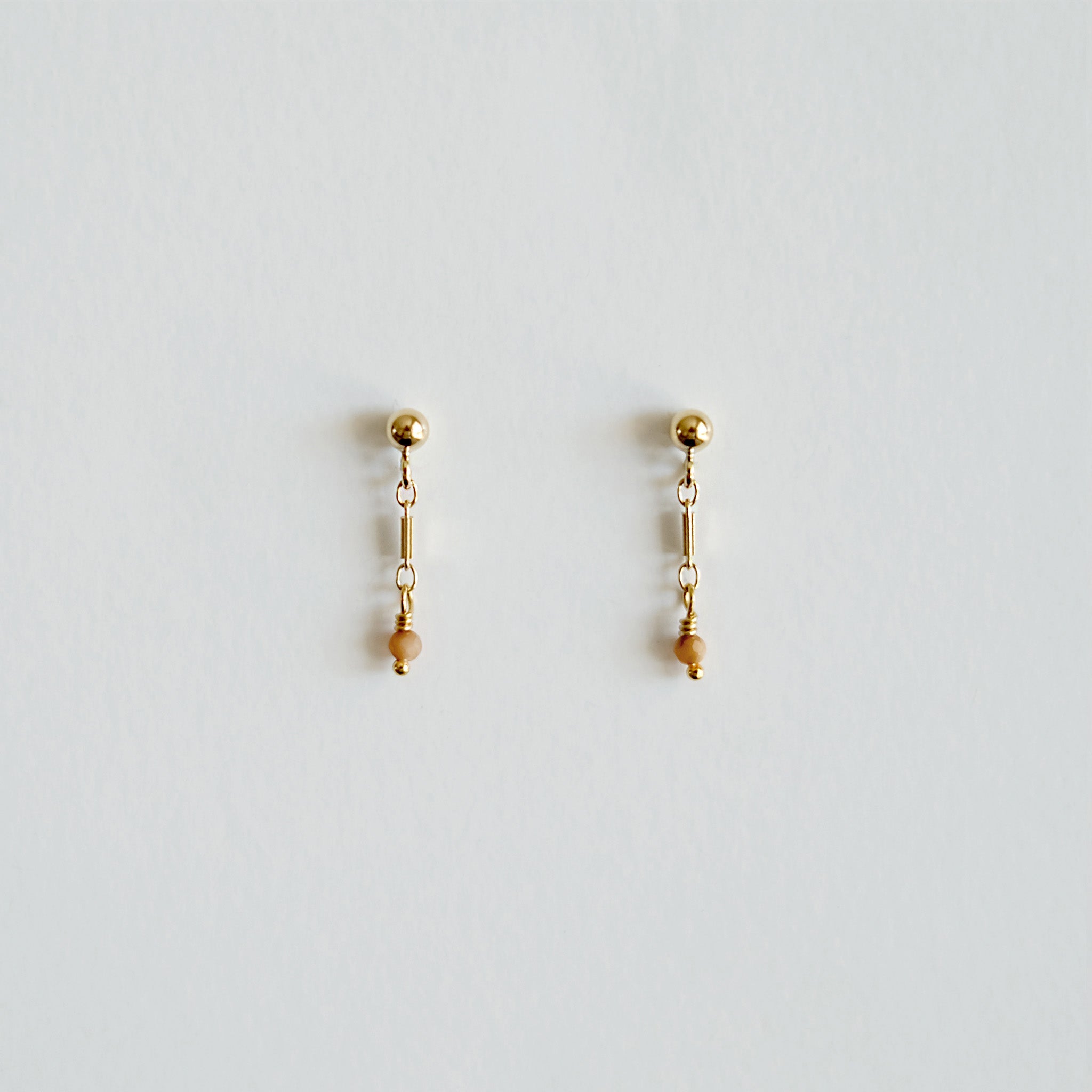 Pair of gold earrings with small beads on a light gray background