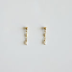 Pair of gold earrings with pearl drops on a light gray background