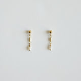 Pair of gold earrings with pearl drops on a light gray background
