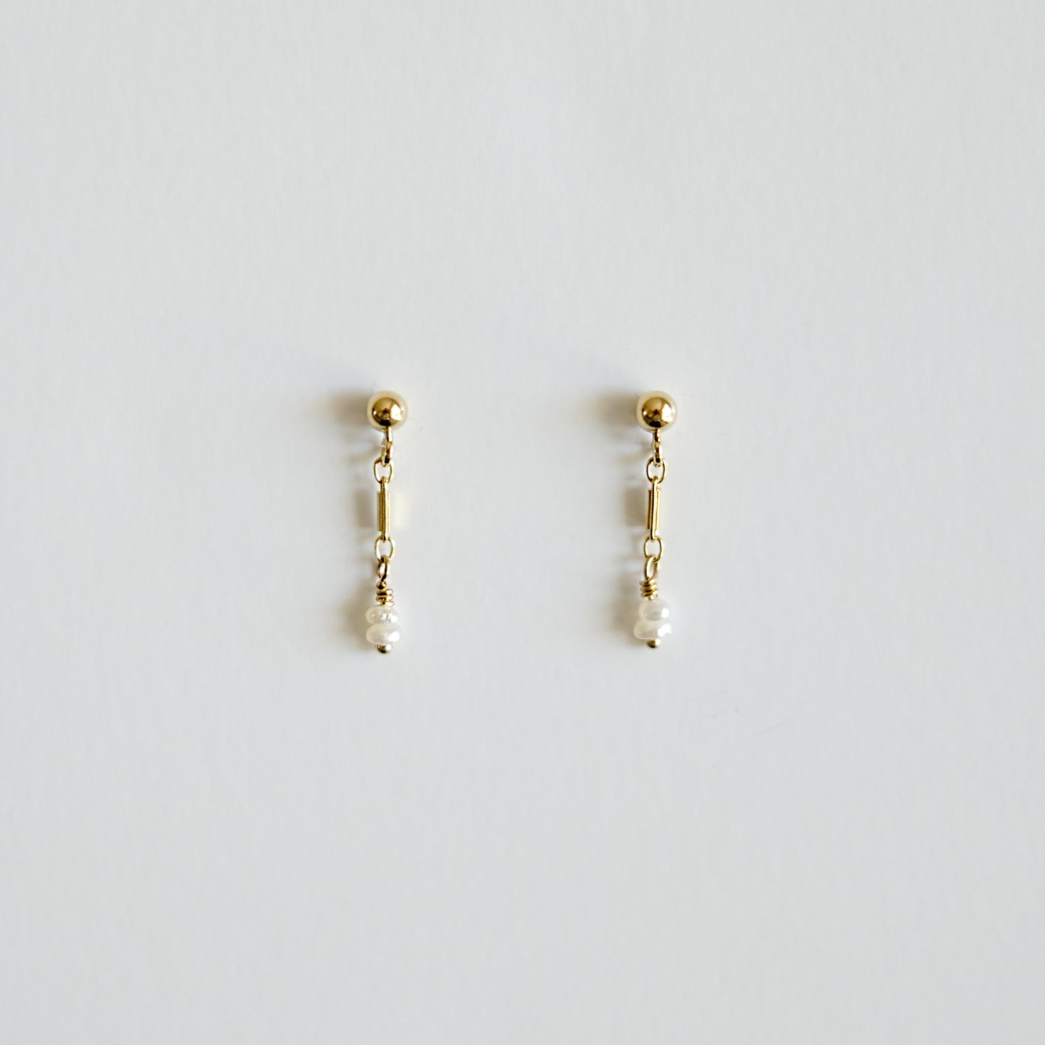 Pair of gold earrings with pearl drops on a light gray background