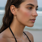 Close-up of a woman wearing gold earrings with a blurred beach background