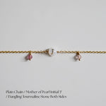 Gold chain bracletlet with mother of pearl initial 'J' and dangling tourmaline stones on a light gray background.