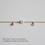 Gold chain bracletlet with mother of pearl initial 'J' and dangling tourmaline stones on a light gray background.
