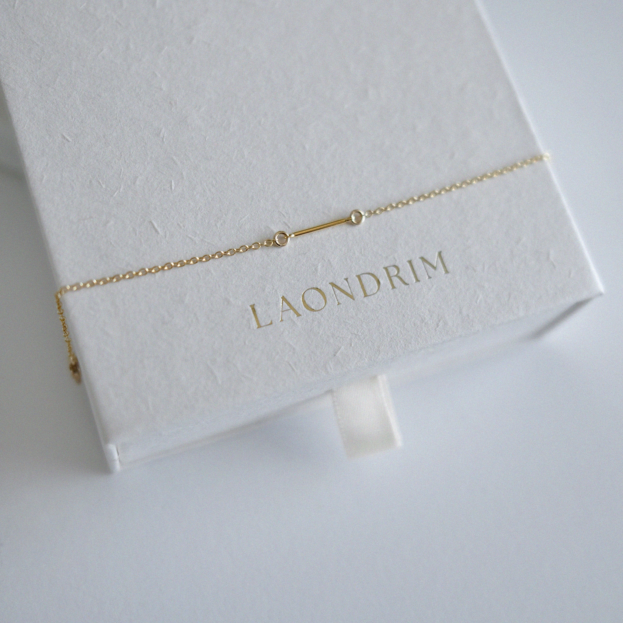 Dainty chain with small bar bracelet on a white box with 'LAONDRIM' branding