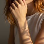 Close-up of a person wearing a delicate gold bracelet on a neutral background