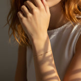 Close-up of a person wearing a delicate gold bracelet on a neutral background