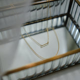 Two gold necklaces on a black metal stand with a blurred background