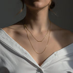 Close-up of a person wearing a delicate gold necklace against a neutral background